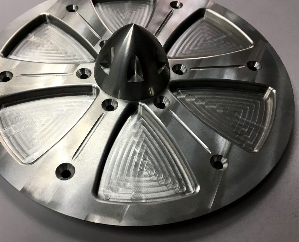Close-up view of a metallic part with triangular patterns and a central cone-like structure.